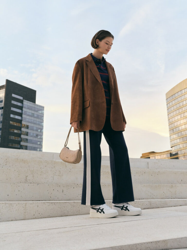 Frau gestylt mit einer Wildlederjacke, Jogginganzug und Sneakers von Asics