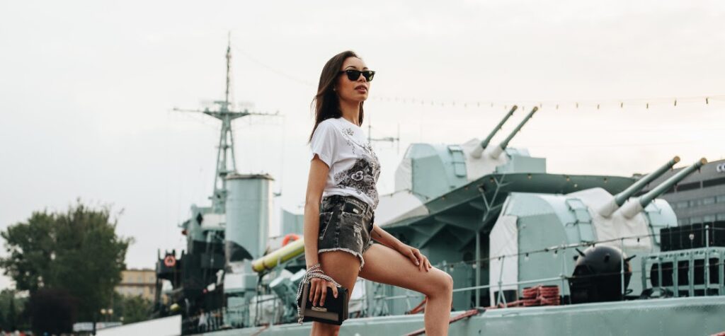 Frau in Shorts, schwarzen Pantoletten, weißem T-Shirt und mit einer kleinen Handtasche