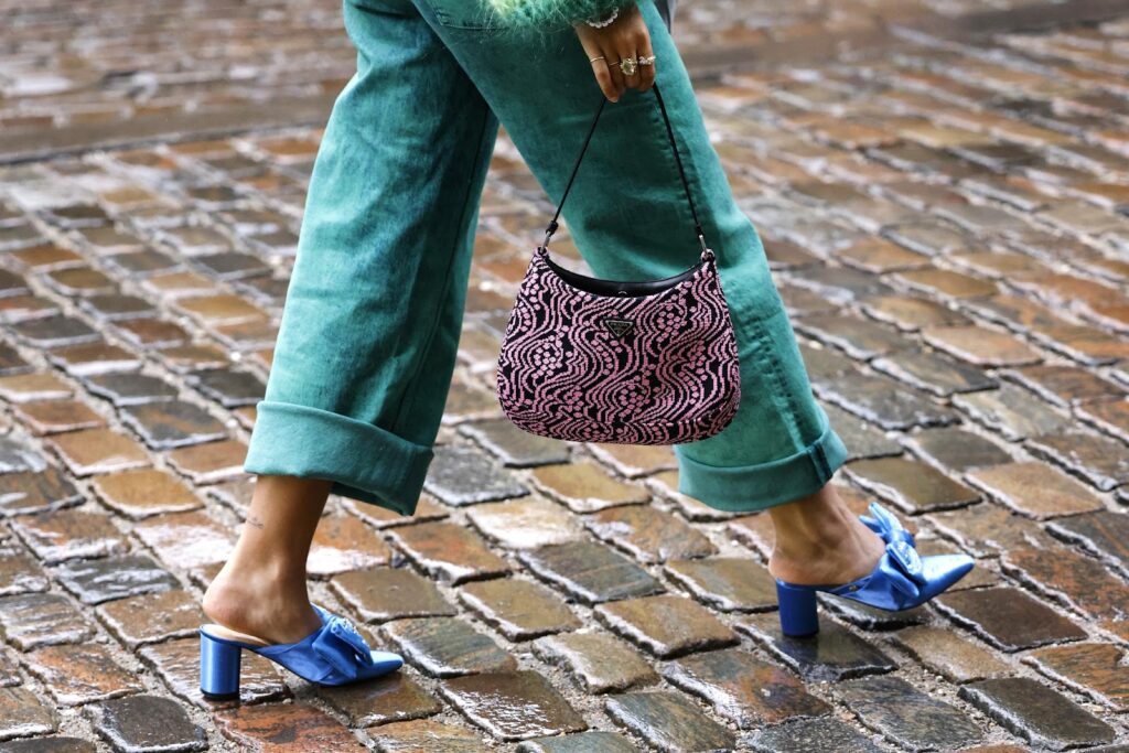 Frau in blauen Pantoletten, einer grünen Hose und mit einer gemusterten Handtasche