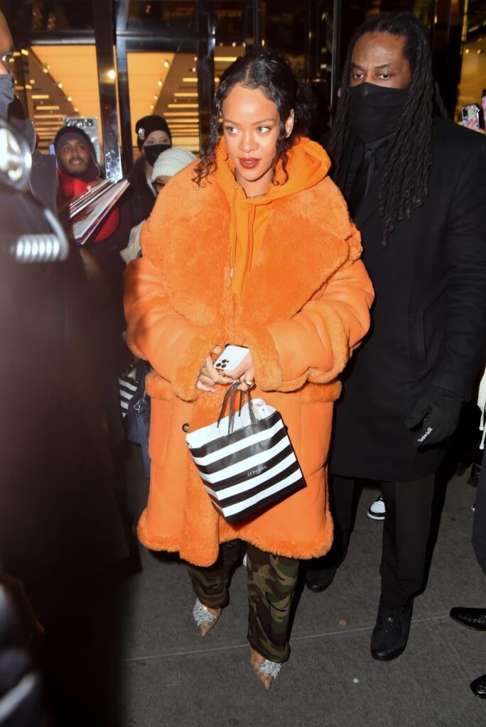Rihanna in Cargohosen im Military-Look, orangefarbenem Hoodie, gleichfarbigem Mantel und Pumps