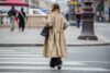 Frau in einem beigefarbenen Trenchcoat geht durch die Straße