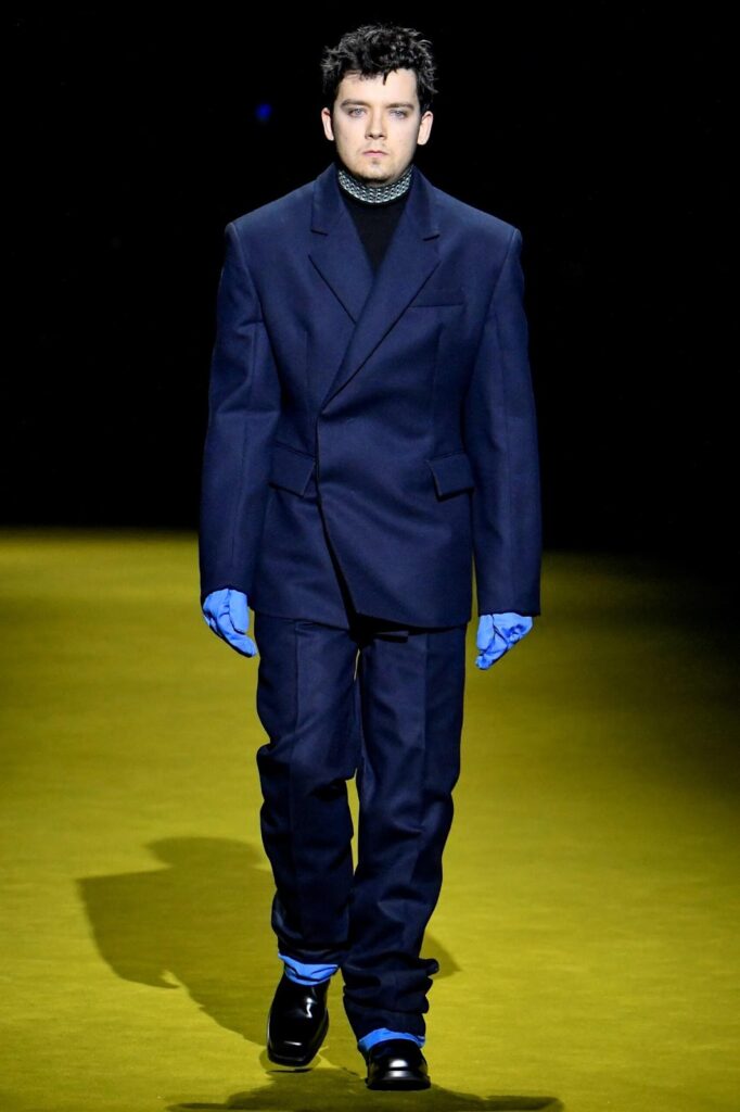 Mann in dunkelblauen Anzug, in blauen Handschuhen und in schwarzen Halbschuhen