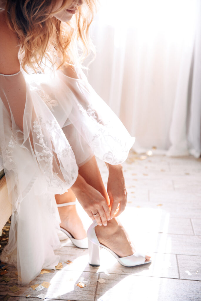Die Braut zieht ihre Hochzeitsschuhe im natürlichen Sonnenlicht an