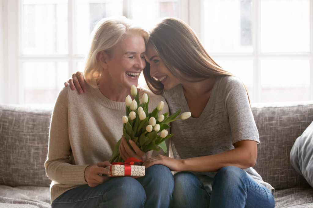 Frau schenkt ihrer Mutter weiße Tulpen und ein kleines Geschenk