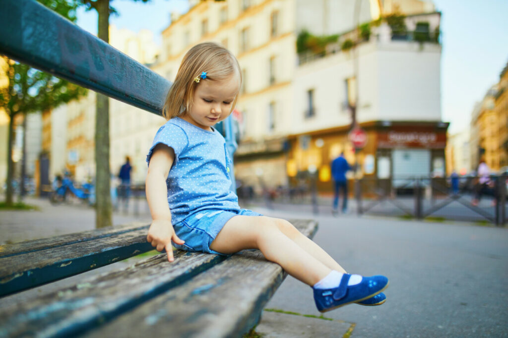 Zweijähriges Mädchen sitzt auf einer Bank in Paris, Frankreich