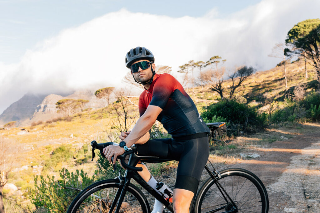 Radfahrer mit Helm und Brille, der mit seinem Fahrrad vor einer wilden Landschaft steht