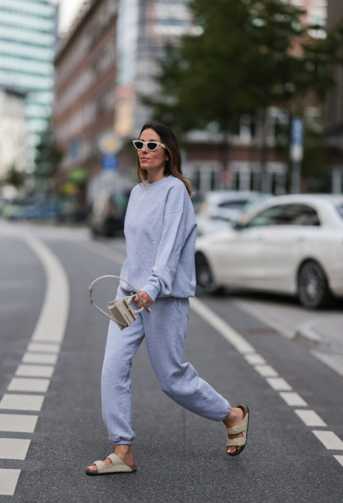 Elise Seitz trägt eine weiße Celine Sonnenbrille, einen grauen Oversize-Pullover von Soho Studios, eine passende graue Jogginghose von Soho Studios, eine weiße Jacquemus Chiquito Mini-Tasche aus Leder und beigefarbene Birkenstock Arizona Pantoletten